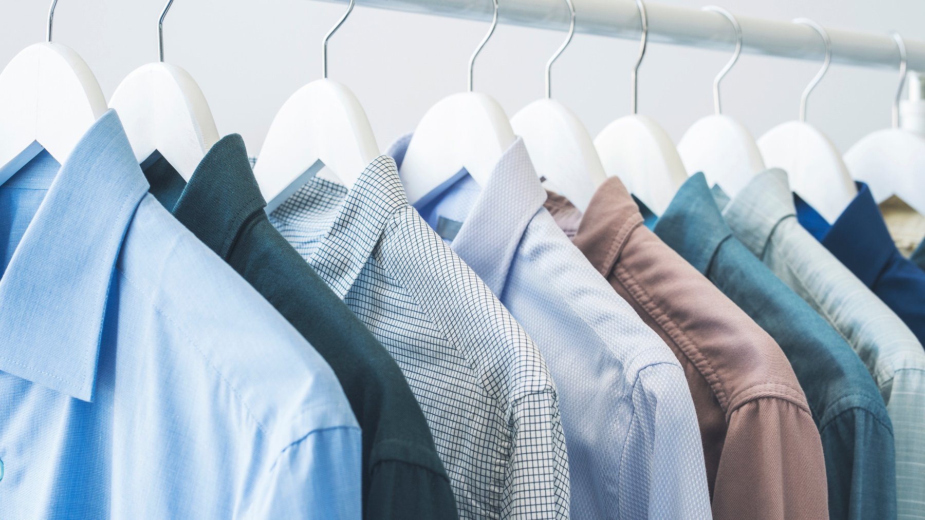 Assorted blue shirts hanging on wooden hangers